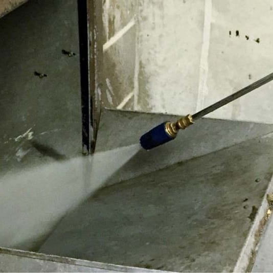 A pressure washer lance spraying hot water down into an open trash chute