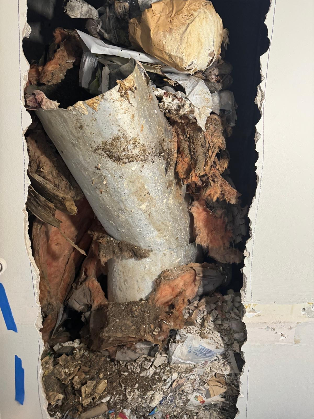 A failed trash chute inside a wall broken open around it